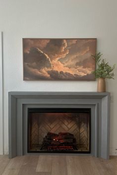 a fire place with a painting on the wall above it and wood flooring below