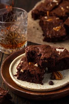 two pieces of chocolate brownie on a plate next to a glass of whiskey and some pecans