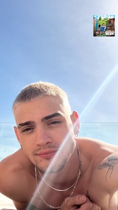 a shirtless man laying on the beach with his hand under his chin and looking at the camera