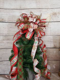 a small christmas tree with red and green ribbons on it's top, sitting in front of a wooden wall