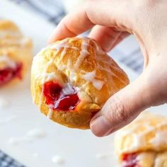 a person holding a pastry with icing and strawberry jam on it in front of other pastries