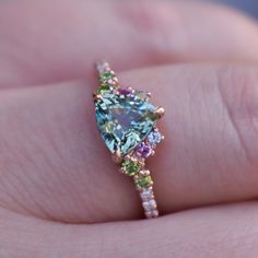 a woman's hand holding a ring with an aqua and multicolored diamond