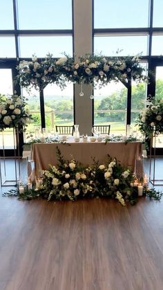 a table with flowers and candles on it in front of large windows at a wedding reception