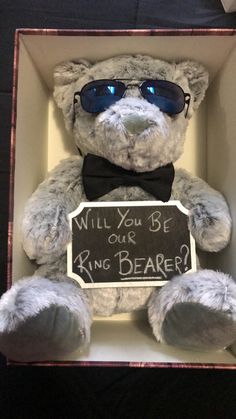 a teddy bear with sunglasses and a sign that says will you be our ring bearer?