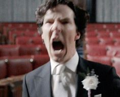 a man in a suit and tie is screaming with his mouth wide open while holding a flower