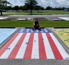 a man sitting on the ground in front of an american flag painted parking lot area