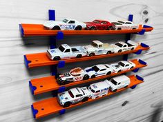 toy cars are lined up on three orange shelving racks against a white wooden wall