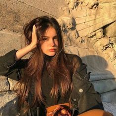 a woman sitting on the ground with her hand in her hair and looking at the camera