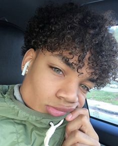 a woman with curly hair sitting in a car looking at the camera and taking a selfie