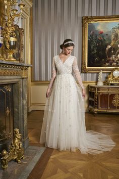 a woman in a white wedding dress standing next to a fireplace and painting on the wall