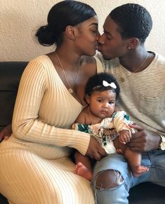 a man and woman sitting on a couch kissing a baby