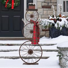 a bicycle made out of an old wheel in front of a house with snow on the ground