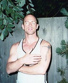 a man standing in front of a fence with his arms crossed and tattoos on his chest