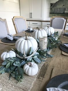 the table is set with white pumpkins and greenery