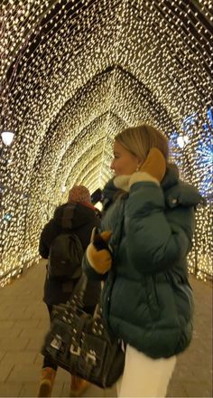 two people are walking through a tunnel covered in christmas lights, one is carrying a handbag and the other is holding a purse