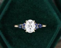 an engagement ring with blue sapphire stones in a green velvet box on top of a carpeted surface