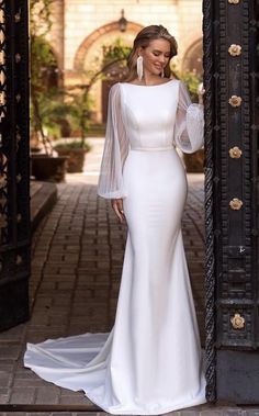 a woman standing in front of an open door wearing a white dress with sheer sleeves