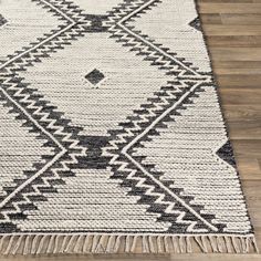 a black and white rug with fringes on top of a wooden floor in a room