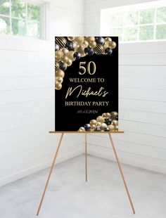 a black and gold 50th birthday party sign on an easel in front of a window