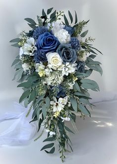 a blue and white bridal bouquet with greenery on the bottom, in front of a white background