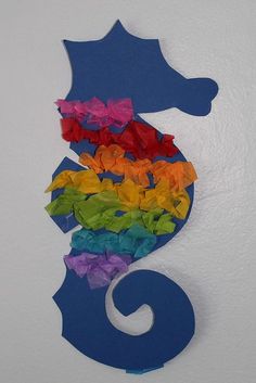 a seahorse made out of tissue paper on a white wall with rainbows in it