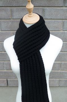 a black knitted scarf sitting on top of a white mannequin