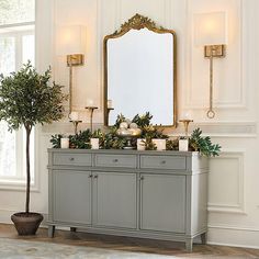 a table with candles, potted plants and a large mirror on the wall above it