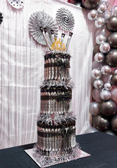 there is a cake made out of wine bottles and silver balloons on the wall behind it