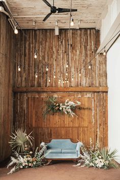 a bride and groom sitting on a couch in front of a wooden wall with hanging lights