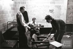 a group of people playing guitars in a room with graffiti on the wall behind them