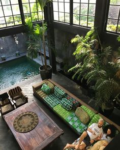 two men sitting on couches in an indoor living room with pool and trees behind them