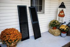 two large black shutters sitting on the side of a house next to flowers and hay bales