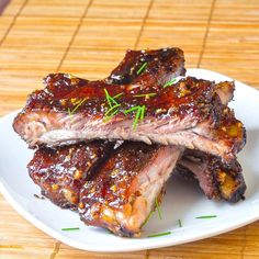 two pieces of barbecue ribs on a white plate with green sprig garnishes