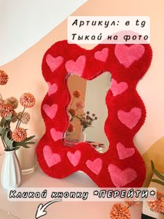 a red heart shaped mirror sitting on top of a table next to vases and flowers