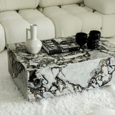 a marble coffee table with two black vases on it and a white couch in the background