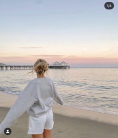 a woman is walking on the beach at sunset