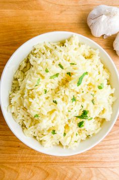 a white bowl filled with rice next to garlic and an onion on a wooden table