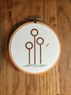 a hand embroidered hoop hanging on a wooden surface with an image of three street lamps