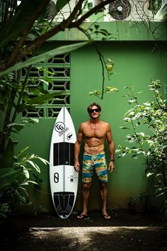 a shirtless man standing next to a surfboard in front of a green wall