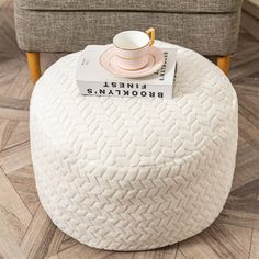 a white ottoman with a book on it and a cup sitting on top of it