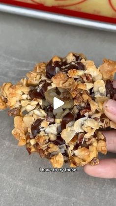 a person holding up a cookie with chocolate chips and nuts on it, in front of a red box