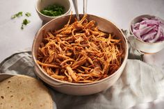 a bowl filled with shredded meat next to two bowls of salsa and tortillas