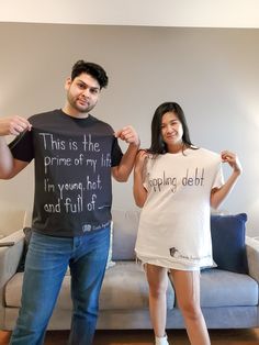 a man and woman standing next to each other in front of a couch holding up t - shirts