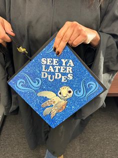 a person holding a blue graduation cap with a sea ya later dude design on it