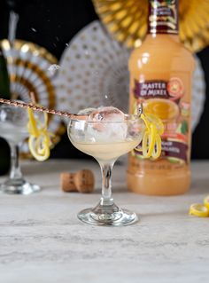 an alcoholic cocktail with lemon garnish in a coupe glass next to two champagne flutes