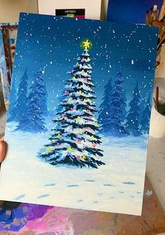 a person holding up a painting of a christmas tree