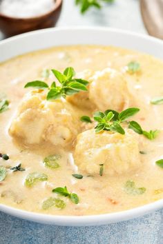 a white bowl filled with meatballs covered in cheese and garnished with green leaves