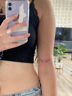 a woman holding up her phone case with an arrow tattoo on the back of her left arm