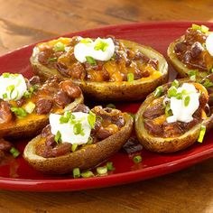 baked potatoes topped with chili and sour cream on a red plate sitting on a wooden table