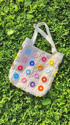 a crocheted bag sitting on top of green grass with flowers in the middle